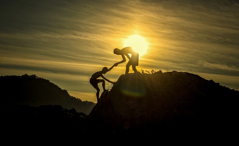 one person helping another over a slope with the sun in the background