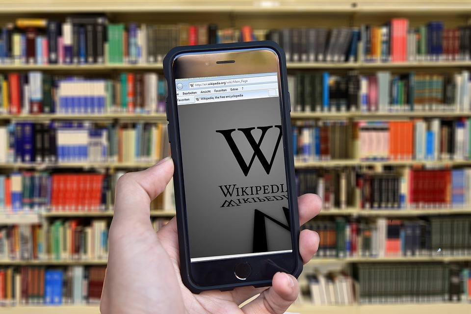 A phone is center screen displaying wikipedia in front of an actual library