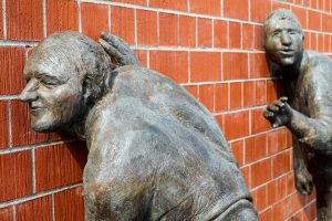 Sculptures of people put their ears to a brick wall, I wonder what they hear